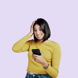 Woman with dark hair, wearing a yellow top is looking at mobile phone she is holding in one hand. Her other hand is to her head. She looks a little stressed and in need of coaching.